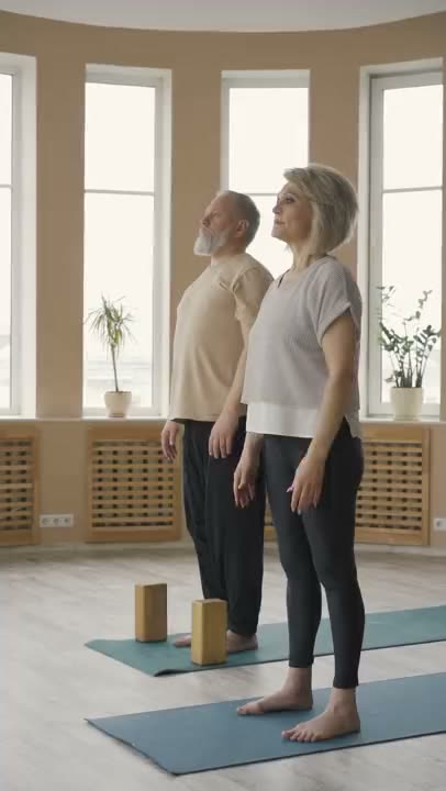 Older couple practicing standing balance exercises on yoga mats in a sunlit studio